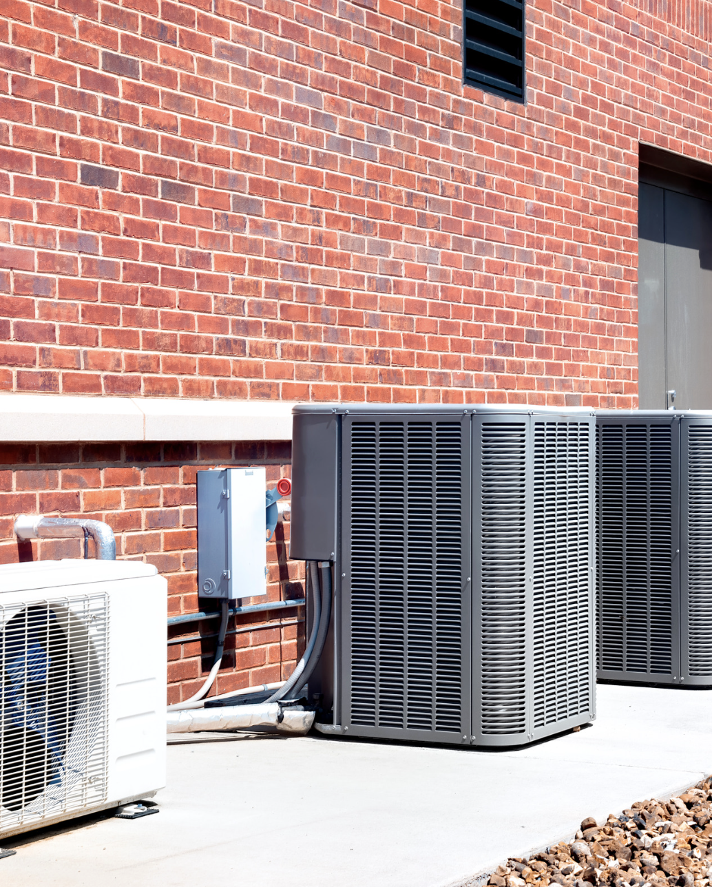 Multiple central A/C units and a mini-split installed along a brick wall